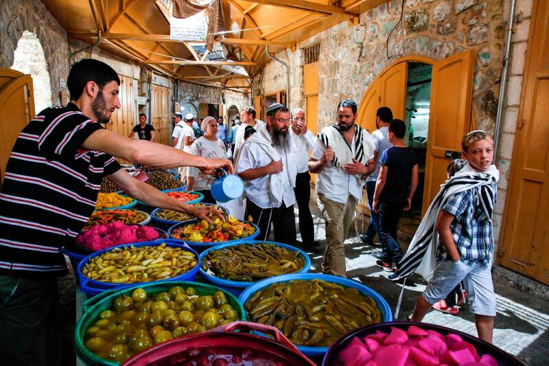 Jewish settlers guarded by Israeli security forces walk past a Palestinian pickled vegetable and olive vendor's stall as they tour the Palestinian side of the old city market in the occupied West Bank city of Hebron. AFP