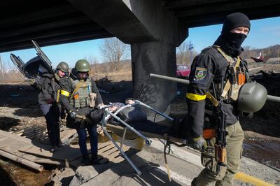 Ukrainians soldiers pass an improvised path under a destroyed bridge as they assist an elderly resident in Irpin. AP