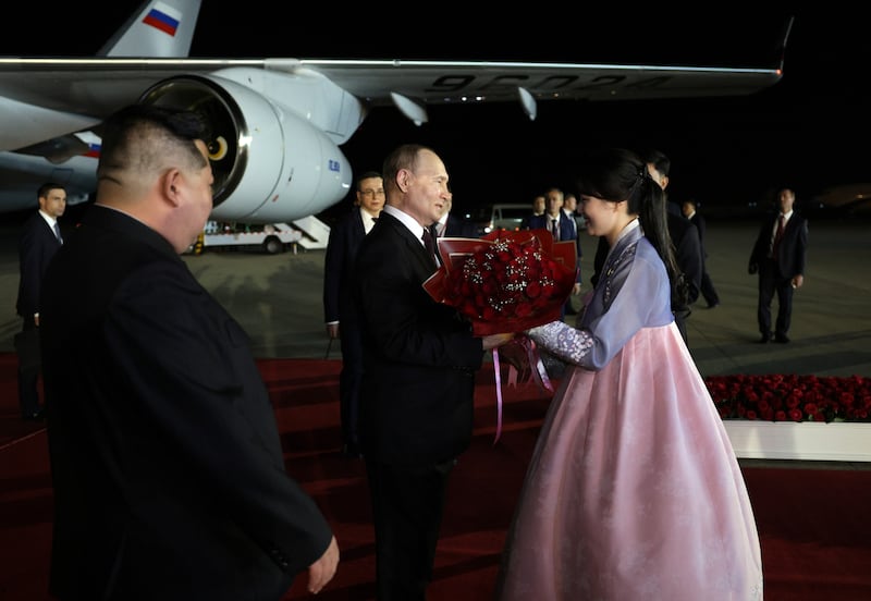 Mr Putin is welcomed with flowers as Mr Kim watches on.  EPA / Sputnik / Kremlin pool
