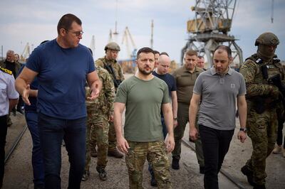 In this photo provided by the Ukrainian Presidential Press Office, Ukrainian President Volodymyr Zelenskyy, center, surrounded by ambassadors of different countries and UN officials, visits a port in Chornomork during loading of grain on a Turkish ship, background, close to Odesa, Ukraine, Friday, July 29, 2022.  (Ukrainian Presidential Press Office via AP)