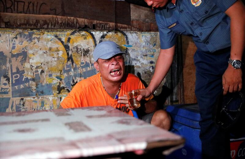 A police officer gives a glass of water to a man as he comforts him after his brother, who police say was killed in a spate of drug-related violence overnight, was shot in Manila, Philippines August 16, 2017. Picture taken August 16, 2017. REUTERS/Dondi Tawatao