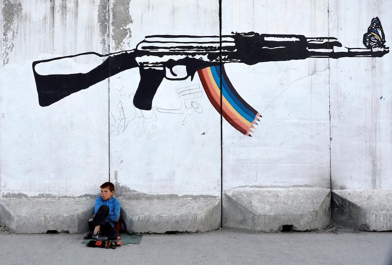 A shoe polisher waits for customers under AK-14 graffiti on a wall in Kabul, Afghanistan. Reuters