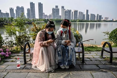 TOPSHOT - Young women wearing facemasks and traditional costumes of Song dynasty and Tang dynasty are seated on a bench in a park next to the East Lake in Wuhan, in China’s central Hubei province on May 17, 2020. Authorities in the pandemic ground zero of Wuhan have ordered mass COVID-19 testing for all 11 million residents after a new cluster of cases emerged over the weekend. / AFP / Hector RETAMAL
