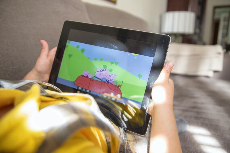 Girl watching cartoons online with the iPad tablet laying in the sofa at home.