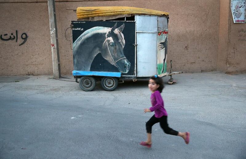 A girl runs past a horse trailer in the old city in the desert town of Yazd.
