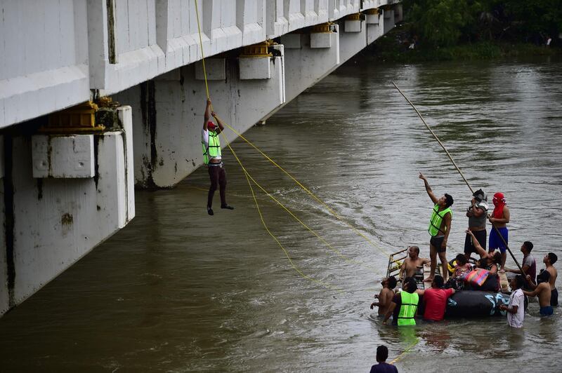 Honduran migrants heading in a caravan to the US, help a fellow man get down to the Suchiate River from the Guatemala-Mexico international border bridge, in Ciudad Hidalgo, Chiapas state, Mexico, on October 20, 2018.  Thousands of migrants who forced their way through Guatemala's northwestern border and flooded onto a bridge leading to Mexico, where riot police battled them back, on Saturday waited at the border in the hope of continuing their journey to the United States. / AFP / Pedro Pardo                    
