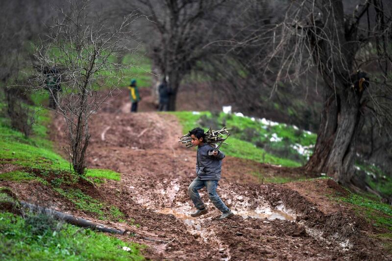 A Syrian boy carries back collected firewood as he returns to a camp for the displaced near Dayr Ballut in the northwest of Aleppo.   AFP