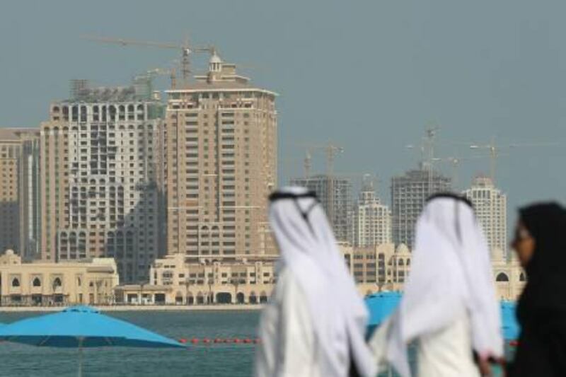 DOHA, QATAR - OCTOBER 30:  People wearing traditional Qatari clothing walk along a beachfront opposite new highrise buildings under construction on the man-made peninsula called The Pearl on October 30, 2010 in Doha, Qatar. The International Monetary Fund (IMF) recently reiterated its projection for the Qatari economy with predictions of double digit growth for 2010 and 2011. Though natural gas and petroleum production are still the biggest two single sources of income, the non-energy sector overtook oil and gas in Qatari GDP for 2009.  (Photo by Sean Gallup/Getty Images) *** Local Caption ***  GYI0062269259.jpg