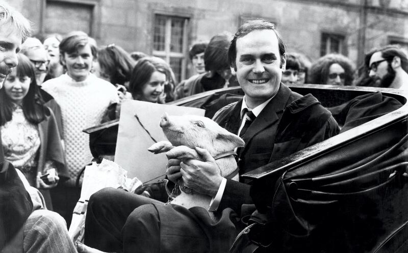 John Cleese at St Andrews ready for a drive around with a piglet. From 1970 to 1973, Cleese served as rector of the University of St Andrews, Fife, Scotland. John Cleese was given the eight week old piglet, by David Steel (Gatehouse of Fleet) and Ronald Sanderson (East Lothian) on behalf of the Porker Club. 20th April 1971. (Photo by Daily Record/Mirrorpix/Mirrorpix via Getty Images)