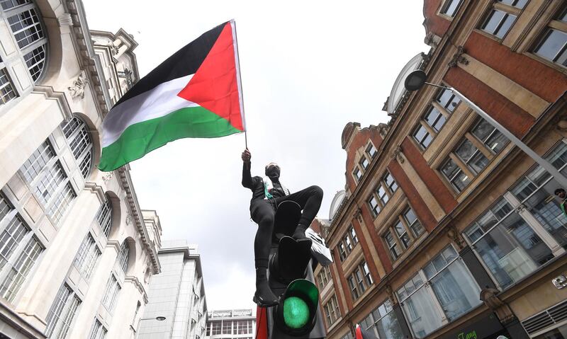 A supporter waves the Palestinian flag from on top of a traffic light during a demonstration outside the Israeli embassy in London, England. EPA
