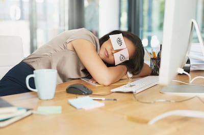 Shot of a tired businesswoman napping at her desk with adhesive notes on her eyes. Getty Images