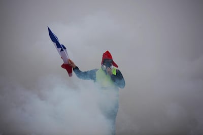 TOPSHOT - A demonstrator holds a French flag as he walks amid the tear gas during a protest of Yellow vests (Gilets jaunes) against rising oil prices and living costs, on December 1, 2018 in Paris.  Anti-government protesters torched dozens of cars and set fire to storefronts during daylong clashes with riot police across central Paris on December 1, as thousands took part in fresh "yellow vest" protests against high fuel taxes. / AFP / -
