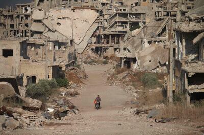 TOPSHOT - A picture taken on August 2, 2018, shows a man riding a motorcycle past destroyed buildings in the opposition-held southern city of Daraa. / AFP PHOTO / Mohamad ABAZEED