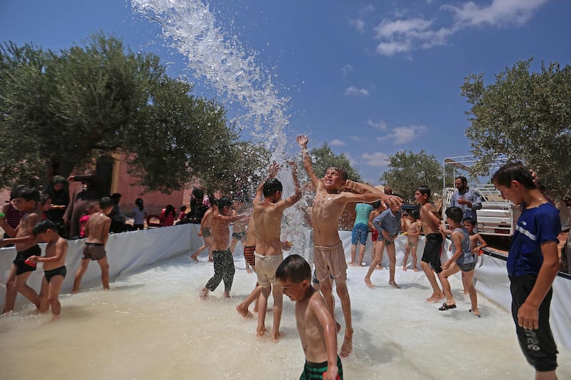 Syrian children play in a portable swimming pool set up by volunteers, at a camp for the displaced in the rebel-held town of Kafr Yahmul in Idlib. 