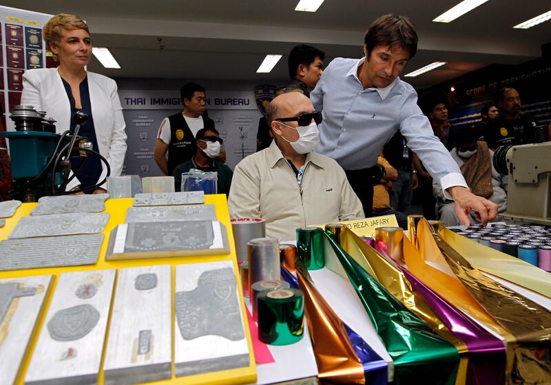 An Interpol agent inspects equipment used to make fake passports. Hamid Reza Jafary, centre, an Iranian citizen, was arrested in 2016 on suspcion of supplying fake passports in Bangkok. EPA