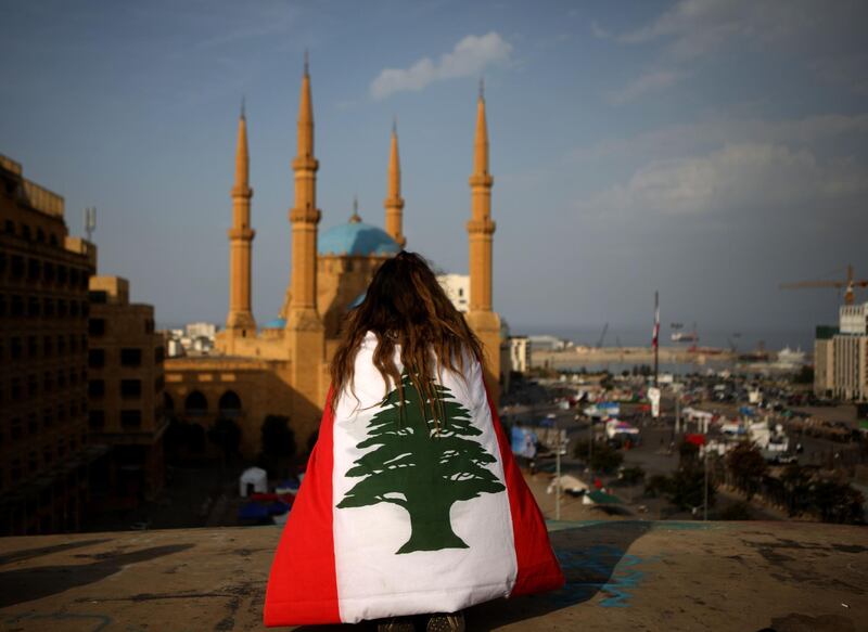 TOPSHOT - A Lebanese anti-government protester, draped in a national flag, sits on the rooftop of 'The Egg' buidling overlooking the Mohammed al-Amin mosque and the Martyrs square in the capital Beirut's downtown district on November 14, 2019. / AFP / Patrick BAZ
