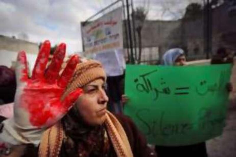 A Palestinian woman holds up a banner reading "Silence = Partnership" in Arabic and English and another holds up her hand with red paint, signifying blood,  as others protest against Israel's military operation in Gaza, outside the U.S. consulate in East Jerusalem, Tuesday, Dec. 30, 2008. Israeli aircraft kept up a relentless string of assaults on Hamas-ruled Gaza on Tuesday, smashing a government complex, security installations and the home of a top militant commander as thousands of Israeli ground troops, backed by tanks and artillery, massed along the border, waiting for a signal to attack. (AP Photo/Dan Balilty) *** Local Caption ***  JRL134_APTOPIX_MIDEAST_ISRAEL_PALESTINIANS.jpg