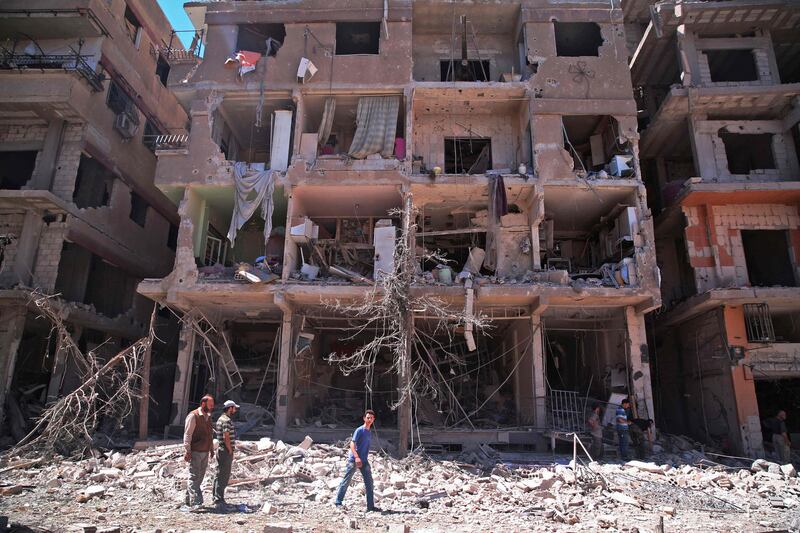 Syrians walk past a damaged building in Ain Tarma, in the eastern Ghouta area, a rebel stronghold east of the capital Damascus on June 21, 2017. / AFP PHOTO / Msallam ABDALBASET