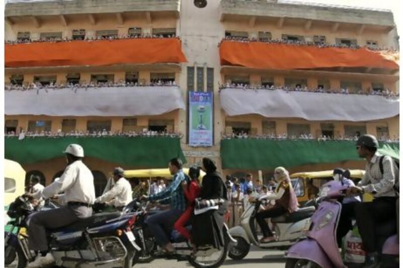 Indian commuters drive past as schoolchildren cheer for the India cricket team from a balcony in Ahmedabad yesterday. Ajit Solanki / AP Photo