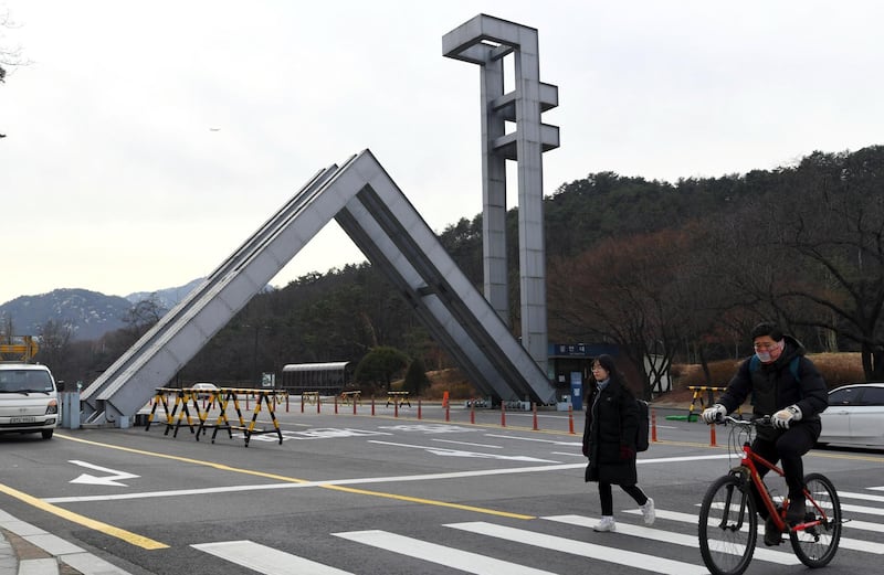 This picture taken on December 14, 2017 shows pedestrians walking in front of the main gate of Seoul National University in southern Seoul. (Photo by JUNG Yeon-Je / AFP)