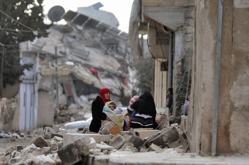 Syrian women and children sit wrapped in blankets outside collapsed buildings on Tuesday in the town of Jandairis, Aleppo province. AFP