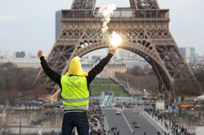 A protester holding a flare gestures in front of the Eiffel Tower during a demonstration in Paris on February 9, 2019, as the "Yellow Vests" (Gilets Jaunes) protesters take to the streets for the 13th consecutive Saturday. - The "Yellow Vests" (Gilets Jaunes) movement in France originally started as a protest about planned fuel hikes but has morphed into a mass protest against the French President's policies and top-down style of governing. (Photo by Zakaria ABDELKAFI / AFP)