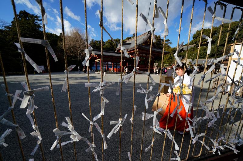 A shrine maiden walks in front of "omikuji," or fortune slips, tied on strings at the Tsurugaoka Hachimangu Shrine in Kamakura, near Tokyo.  Omikuji is a piece of paper written with fortunes on it. Shizuo Kambayashi / AP Photo.