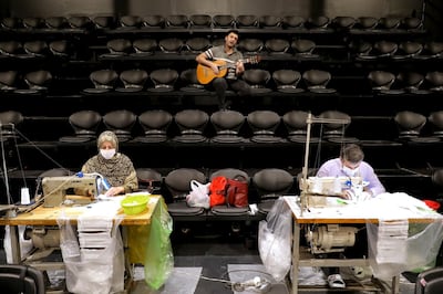 Volunteers wearing face masks to curb the spread of the new coronavirus, sew face masks, as a guitarist plays guitar for volunteers, at the Hafez theatre hall in downtown Tehran, Iran, Wednesday, April 15, 2020. (AP Photo/Ebrahim Noroozi)