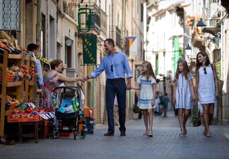 Spanish King Felipe VI, left, shakes hands with a woman as he walks down a street with his wife Queen Letizia, right, and their daughters Spanish crown princess Leonor, second left,  and princess Sofia in the village of Soller on Mallorca islan. Jaime Reina / AFP