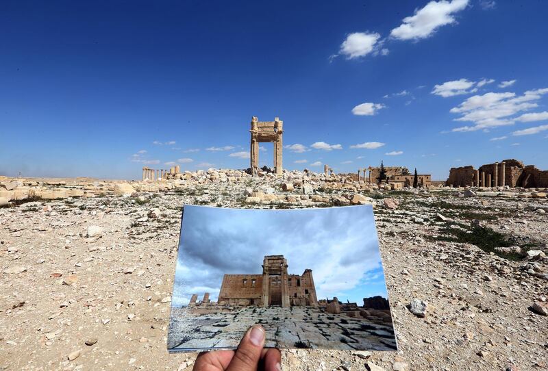 A general view taken on March 31, 2016 shows a photographer holding his picture of the Temple of Bel taken on March 14, 2014 in front of the remains of the historic temple after it was destroyed by Islamic State (IS) group jihadists in September 2015 in the ancient Syrian city of Palmyra. - Syrian troops backed by Russian forces recaptured Palmyra on March 27, 2016, after a fierce offensive to rescue the city from jihadists who view the UNESCO-listed site's magnificent ruins as idolatrous. (Photo by JOSEPH EID / AFP)