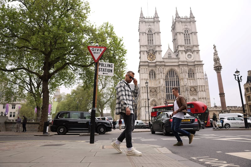 A tourist poses for a photo underneath a polling station sign near Westminster Abbey during local elections in London. Reuters