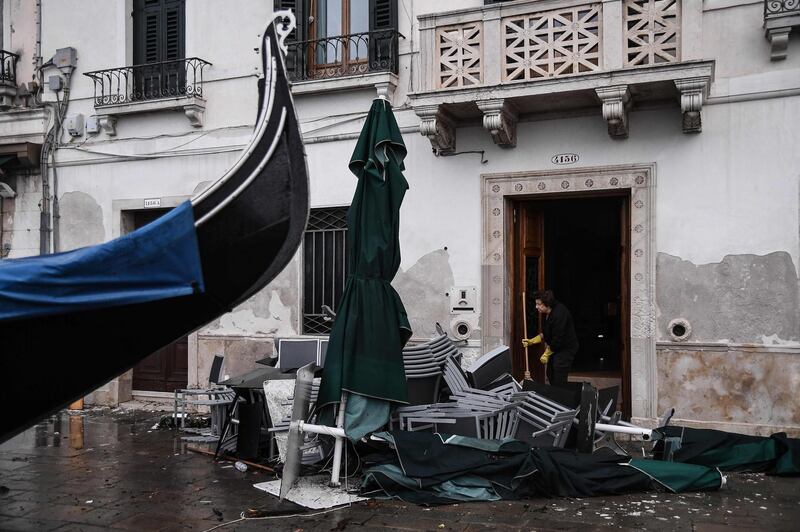 A woman clears a building entrance by piled-up cafe furniture and a stranded gondola. AFP