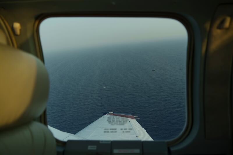 A small migrant boat and a Libyan merchant vessel are visible through the window of the humanitarian aircraft, above the Mediterranean Sea between Libya and Italy.