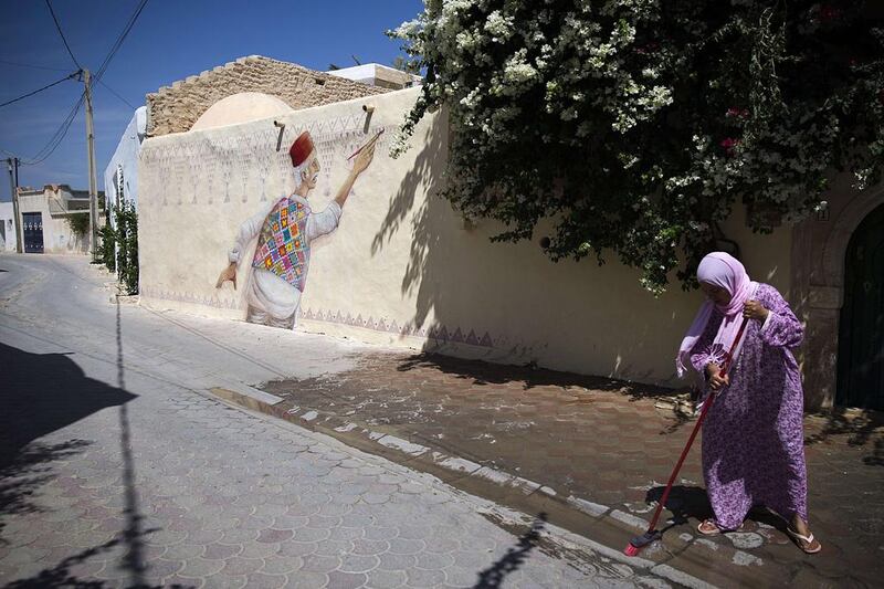 A woman sweeps the street next to a mural by Portuguese artist Mario Belem in the village of Erriadh, on the Tunisian island of Djerba. Joel Saget / AFP Photo