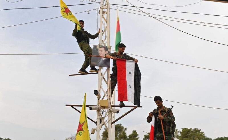 Syrian government soldiers climb up an electrical pole with the Syrian government national flag and the Kurdish People's Protection Units (YPG) yellow flag, along with a portrait of Syrian President Bashar Al Assad, by the Turkish border in the Syrian Kurdish town of Kobane. AFP