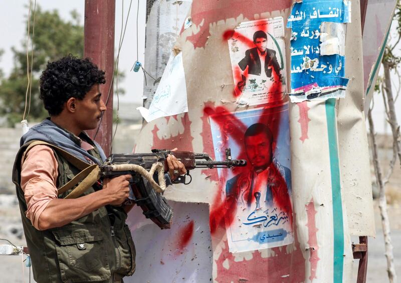 A Yemeni fighter from the Amalqa ("Giants") Brigades loyal to the Saudi-backed government stands pointing a Kalashnikov assault rifle towards a crossed-out plastered poster of the Houthi rebel leader Abdulmalik al-Houthi, on the southern outskirts of the Red Sea port city of Hodeidah near the airport on June 21, 2018. Saleh Al-Obeidi / AFP