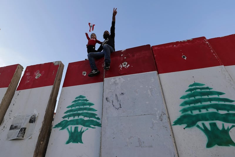 An anti-government protester and his daughter stand on a concrete wall installed by authorities to keep protesters far from the main Lebanese government headquarters and open road to parliament. AP