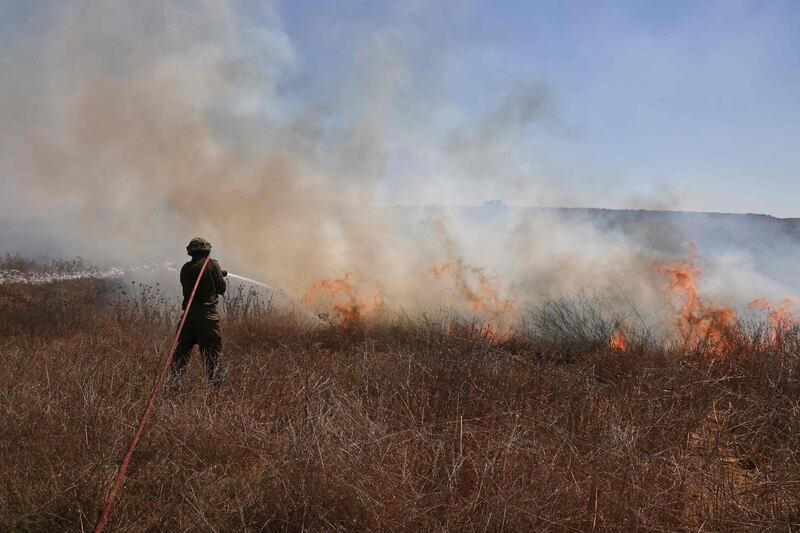 An Israeli soldier extinguishes a fire in a field close to the southern kibbutz of Nir Am near the border with the Gaza Strip on August 25, 2020, after it was set off by incendiary balloons launched from the Palestinian enclave. / AFP / menahem kahana
