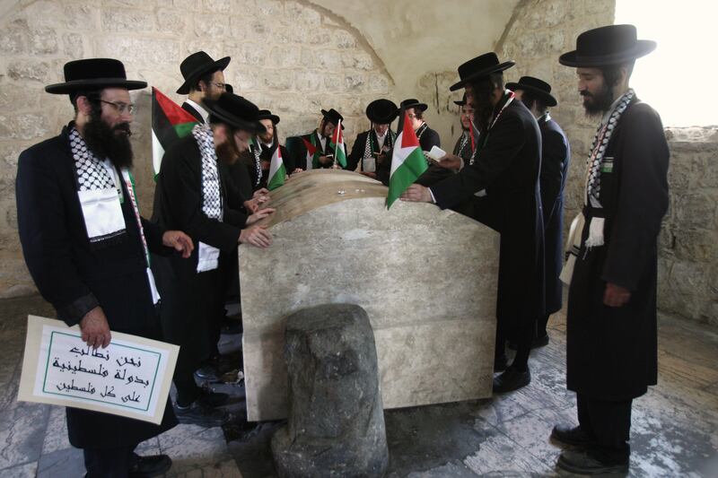 A member of the radical ultra-Orthodox Jewish Neturei Karta anti-Zionist sect holds a sign reading in Arabic: "We ask for a Palestinian state on all of Palestine", as he and others hold Palestinian flags and pray at Joseph's Tomb in the West Bank city of Nablus, Wednesday, Sept. 21, 2011.  Thousands of flag-waving Palestinians rallied Wednesday in towns across the West Bank to show support for their president's bid to win U.N. recognition of a Palestinian state. (AP Photo/Nasser Ishtayeh) *** Local Caption ***  Mideast Israel Palestinians.JPEG-07626.jpg