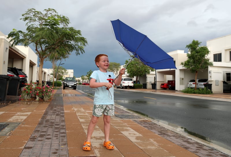 A young boy's attempts to shelter from the rain are foiled by high winds in Dubai. Chris Whiteoak / The National