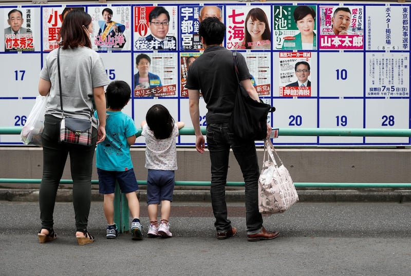 A family considers candidate posters, including current governor Yuriko Koike, for the Tokyo Governor election in front of a voting station in Tokyo, Japan. Reuters