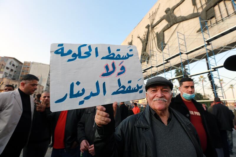 epa08898404 An Iraqi protester carries a plascard reading in Arabic 'Down the government and the dinar does not fall' during a protest at the al-Tahrir square in central Baghdad, Iraq on 21 December 2020. The Iraqi ministry of finance announced that the Iraqi government decided to reduce the value of the Iraqi dinar to be 1,450 dinars per one US dollar in the central bank, instead of its previous price of 1,119 dinars per dollar, in response to a severe liquidity crisis that resulted in the government being unable to pay employees' salaries.  EPA/AHMED JALIL