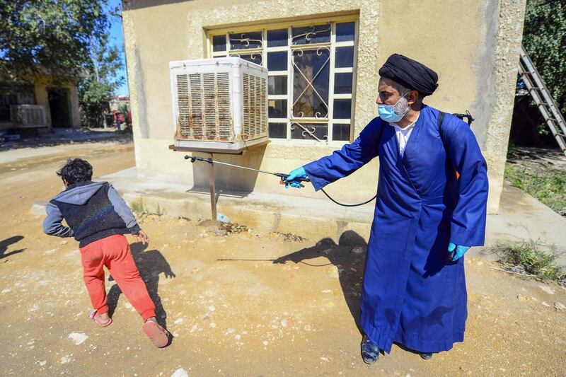 A Shiite cleric sprays disinfectant over a boy in a neighbourhood in the central Iraqi holy city of Najaf. AFP