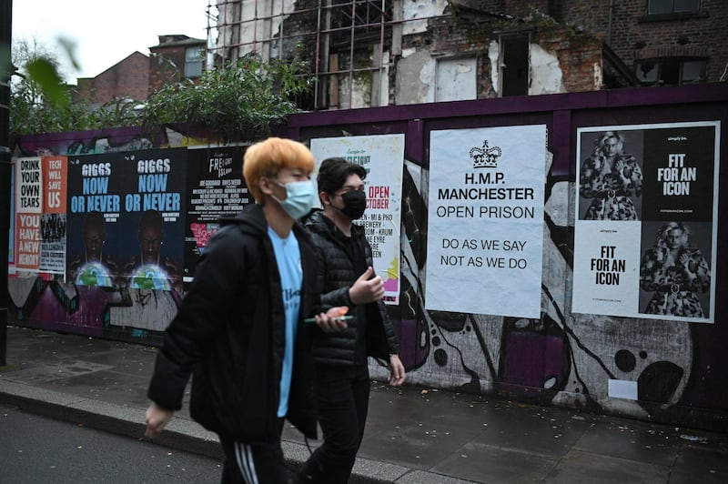 Pedestrians wearing a mask because of the coronavirus pandemic walk past a poster complaining about the second lockdown in Manchester, northwest England on November 10, 2020.  / AFP / Oli SCARFF
