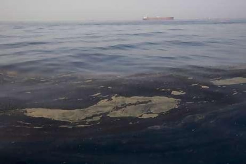 With a tanker of oil in the background, oil from a spill floats on the surface of the sea off the coast of Fujairah.