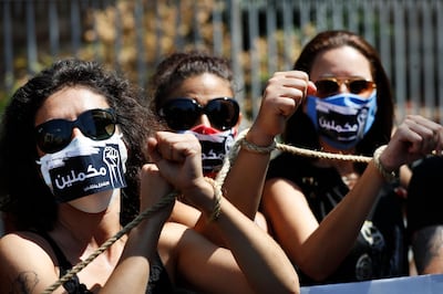 Lebanese anti-government activists handcuff their hands by rope with Arabic stickers on their mouths that read:"We will continue," as they protest outside a Lebanese court demanding the improving judicial independence, in Beirut, Lebanon, Wednesday, June 17, 2020. A year after anti-government protests roiled Lebanon, dozens of protesters are being tried before military courts that human rights lawyers say grossly violate due process and fail to investigate allegations of torture and abuse. (AP Photo/Hussein Malla)