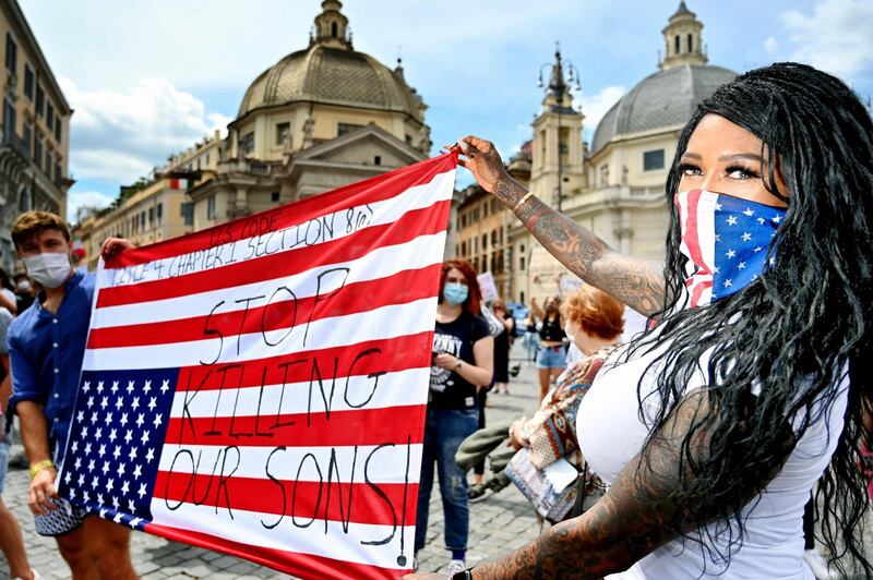 Protesters hold the United States flag upside-down bearing a slogan during a rally in solidarity with the Black Lives Matter movement on the Piazza del Popolo in Rome.   AFP