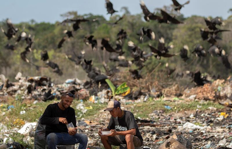 Venezuelans are seen in the municipal garbage dump eating as a flock of vultures is seen in the background in the city of Pacaraima, Brazil.  EPA