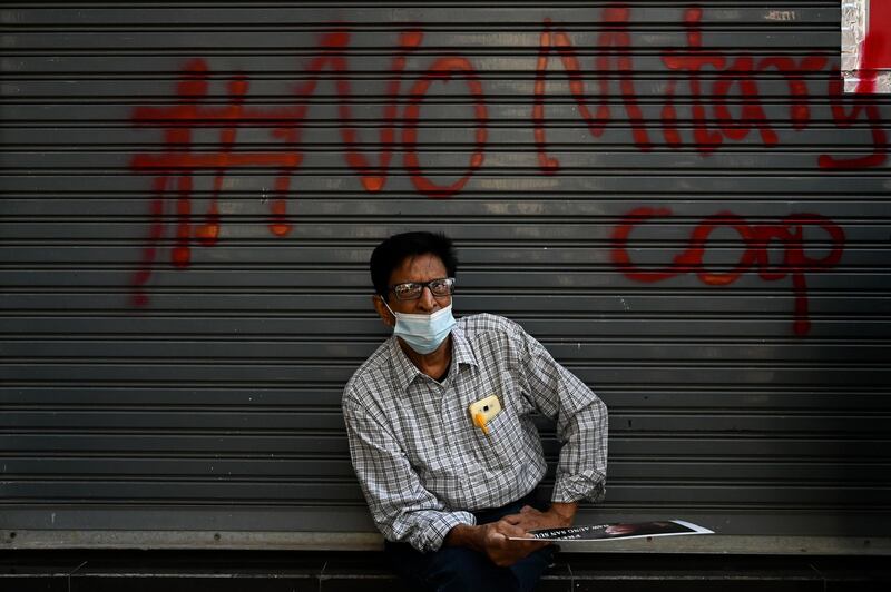 A protester sits in front a graffiti during a demonstration against the military coup in Yangon. AFP