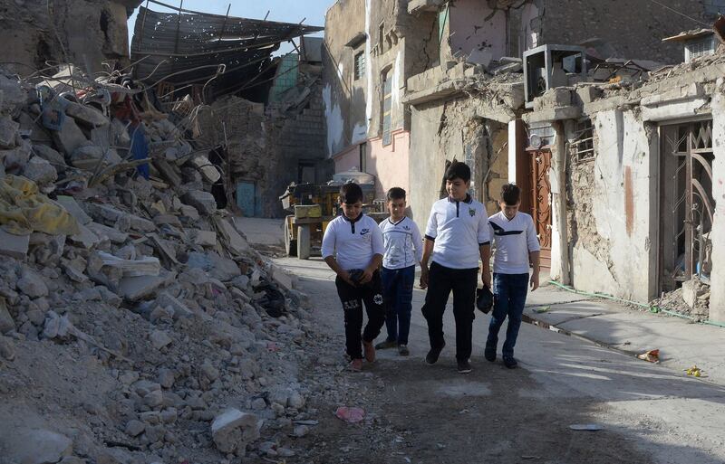 Iraqi schoolboys walk through a narrow street past damaged houses on their way to school in the old city of Mosul in northern Iraq on October 4, 2018. Iraq's second city Mosul was a bastion of the Islamic State group (IS) for three years before the jihadists were driven out in 2017. / AFP / Zaid AL-OBEIDI
